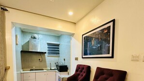 A compact kitchen with modern appliances, two dark bar stools, and a framed cityscape picture on the wall. - EXTACODE APARTMENT (Abuja)