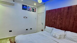 A bedroom with a large bed, a wooden headboard, and a ceiling light fixture. - EXTACODE APARTMENT (Abuja)