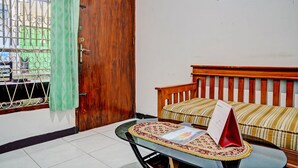 Ein Zimmer mit Holztür, einem Fenster mit Metallgitter, einer Couch mit gestreifter Kissen und einem Kalender auf einem Tisch.