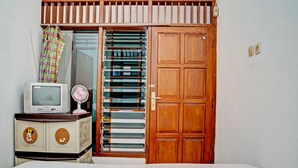 Ein Zimmer mit einem Bett, einem Fernseher auf einer Kommode, einer Holztür und einem Fenster mit Jalousien.