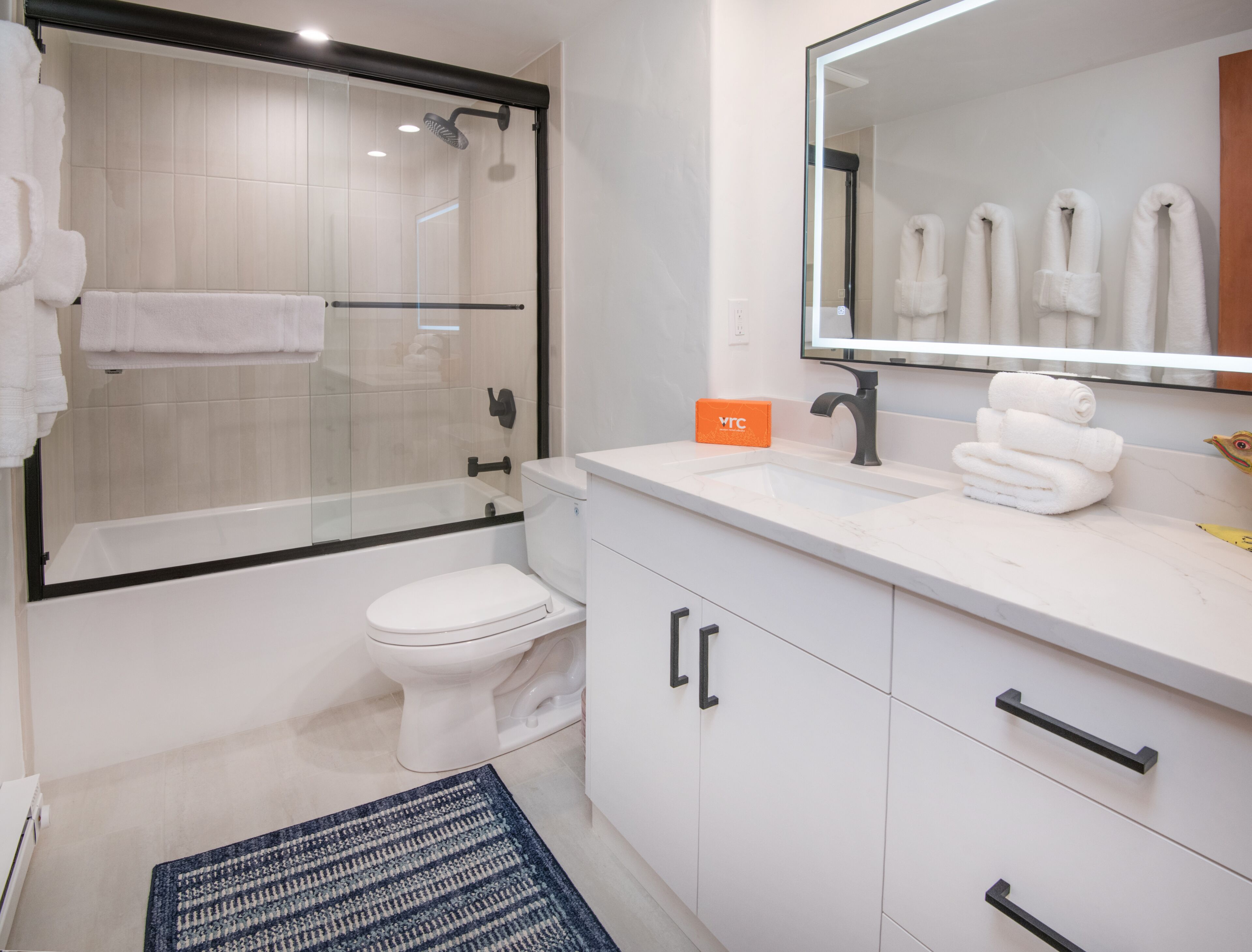 A modern bathroom with a glass-enclosed shower, a white toilet, a sink with a mirror, and neatly folded towels on the counter.