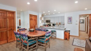 A spacious kitchen with a central island, wooden cabinets, and a dining area with a round table and colorful chairs.