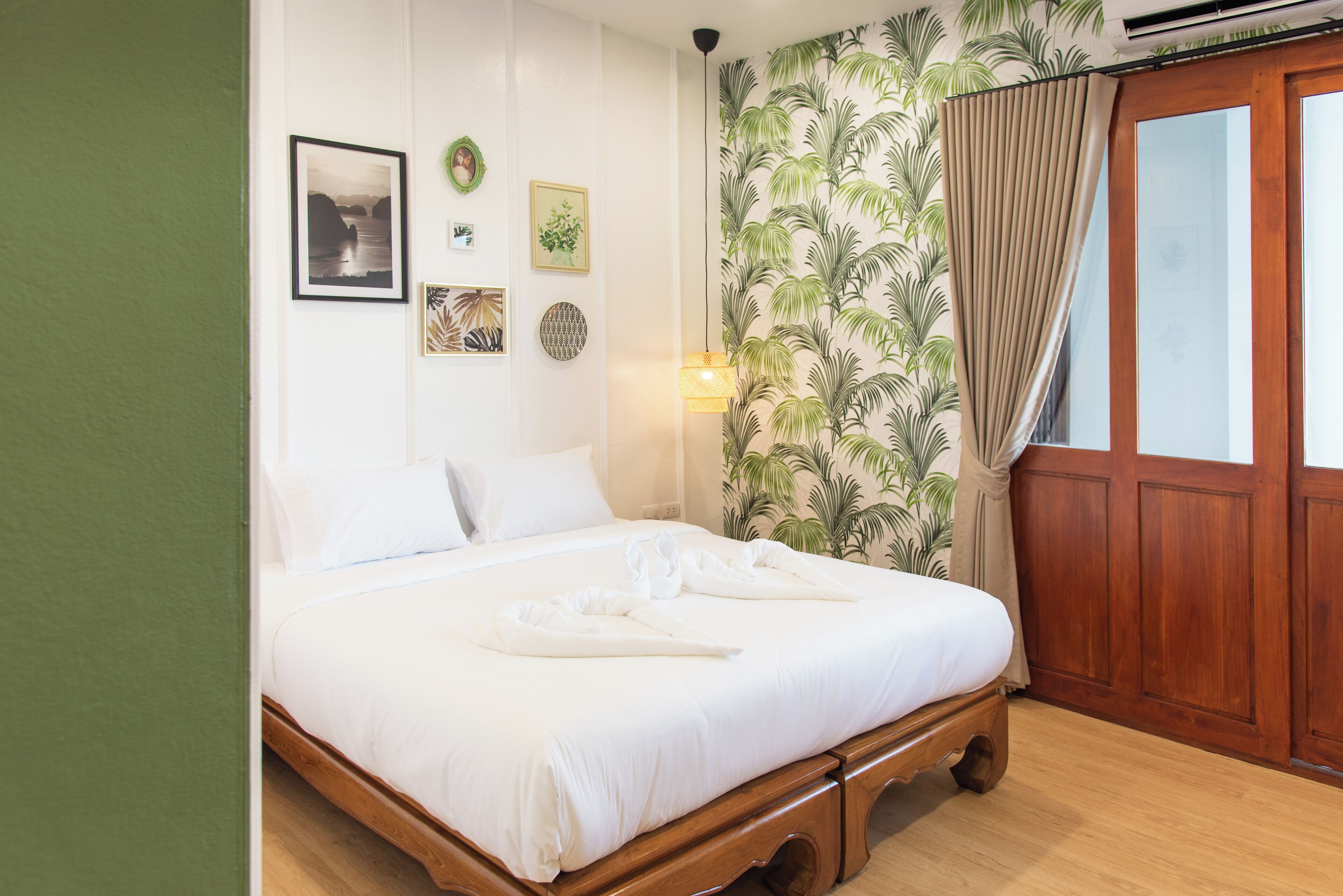 A neatly made bed with white linens, a wooden headboard, and a tropical wallpaper design.