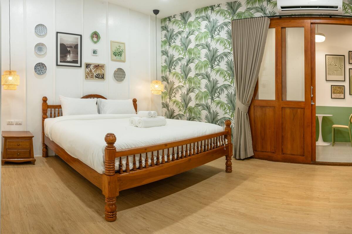 A neatly arranged bedroom with a wooden bed, a bedside table, a wall-mounted air conditioner, and a green-themed wallpaper.
