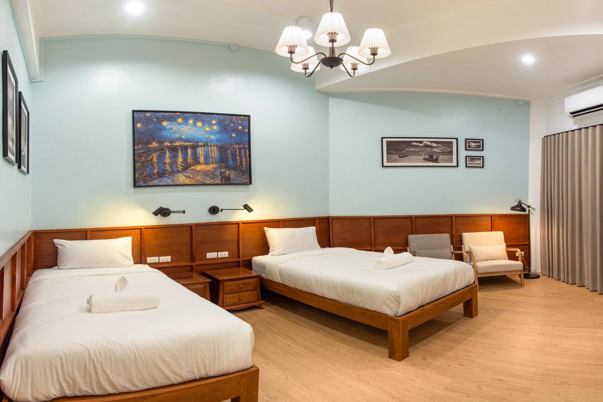 A hotel room with two beds, wooden headboards, a chandelier, and artwork on the walls.