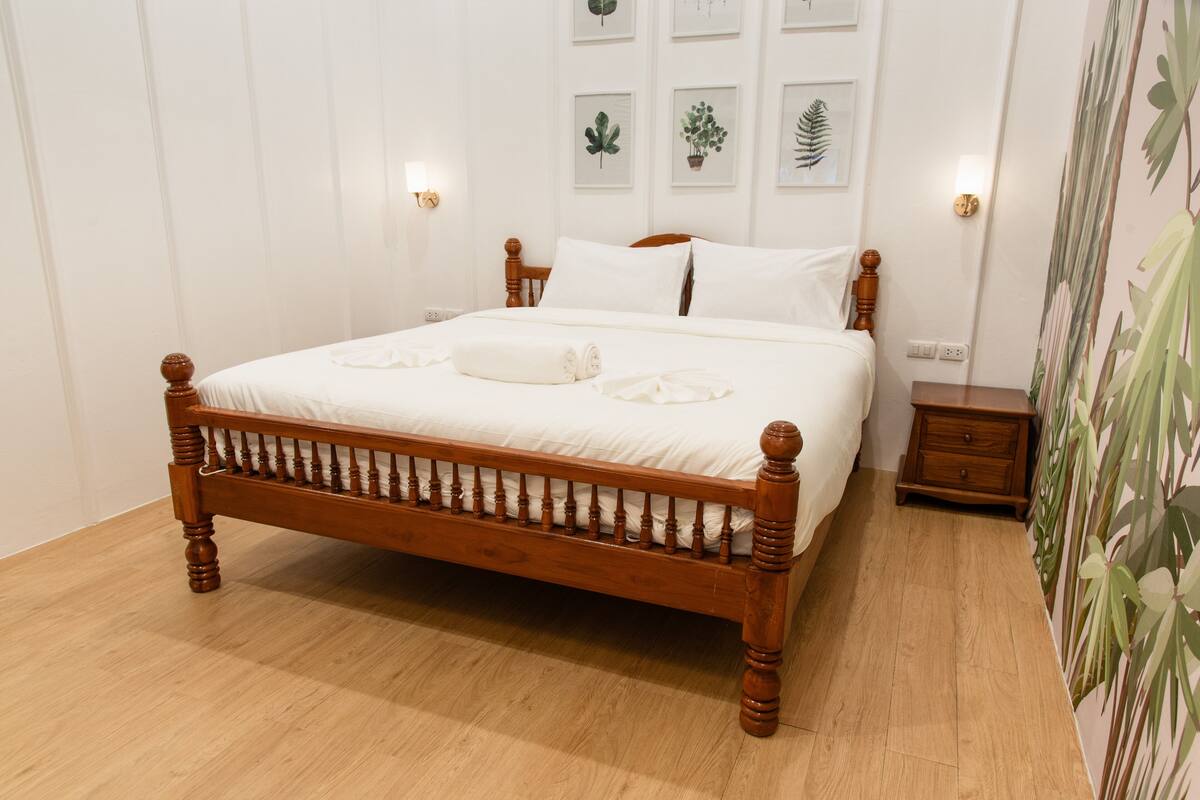 A wooden bed with white bedding, a wooden nightstand, and a wall with framed botanical prints.