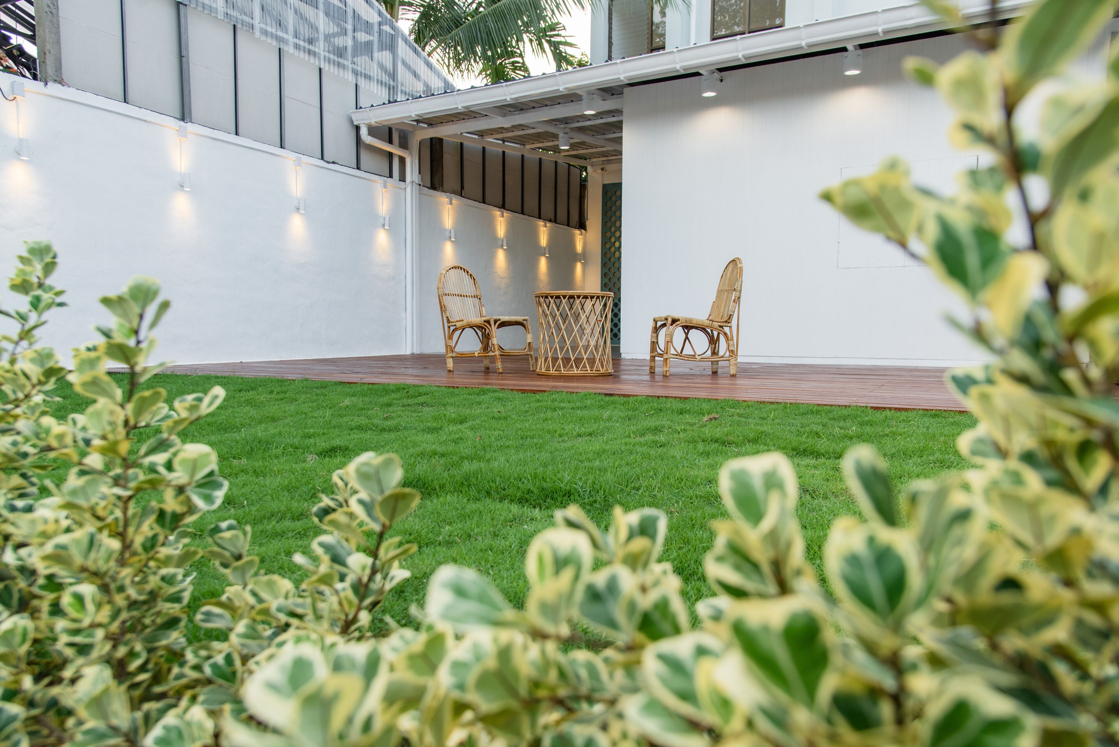 A modern outdoor patio with a wooden deck, two wicker chairs, and a small table.