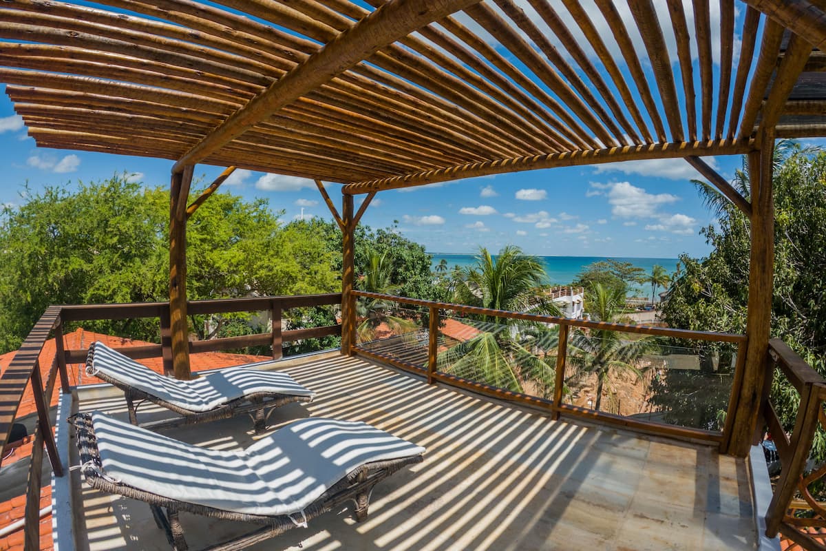 A wooden deck with two striped lounge chairs and a view of the ocean.