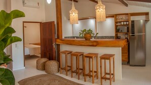 Una cocina moderna con barra de madera, taburetes de bar, refrigerador y luces colgantes.