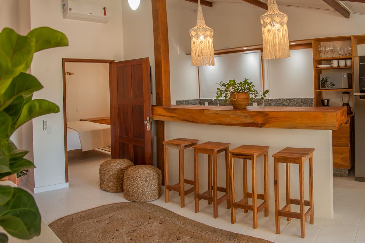 A modern kitchen with a wooden bar, bar stools, a refrigerator, and hanging lights.
