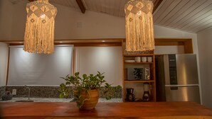 Una cocina con encimera de madera, una planta en maceta, un refrigerador de acero inoxidable y dos lámparas colgantes.