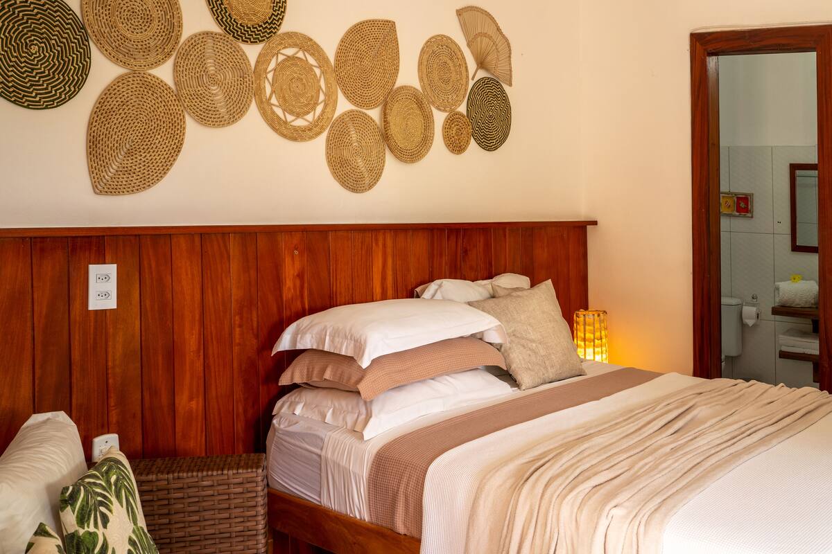 A neatly made bed with multiple pillows and a blanket, a wooden headboard, and a wall decorated with woven baskets.