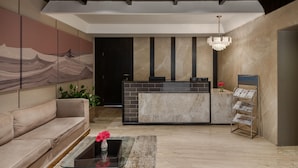 A modern reception area with a marble reception desk, a sofa, a glass coffee table with a vase, and a chandelier. - Voyage Milestone Hotel & Banquet Siliguri (Jalpaiguri)