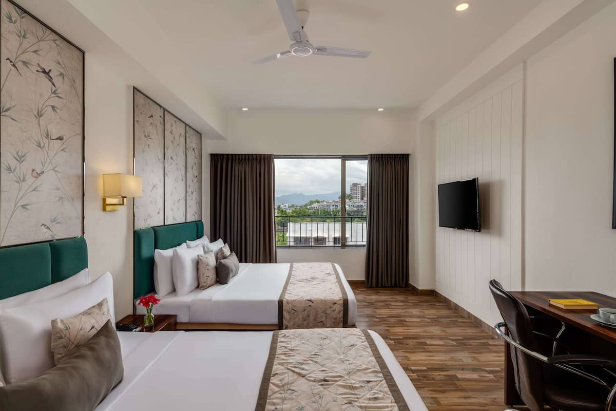 A hotel room with two beds, a desk, a chair, a TV, and a balcony with a view.