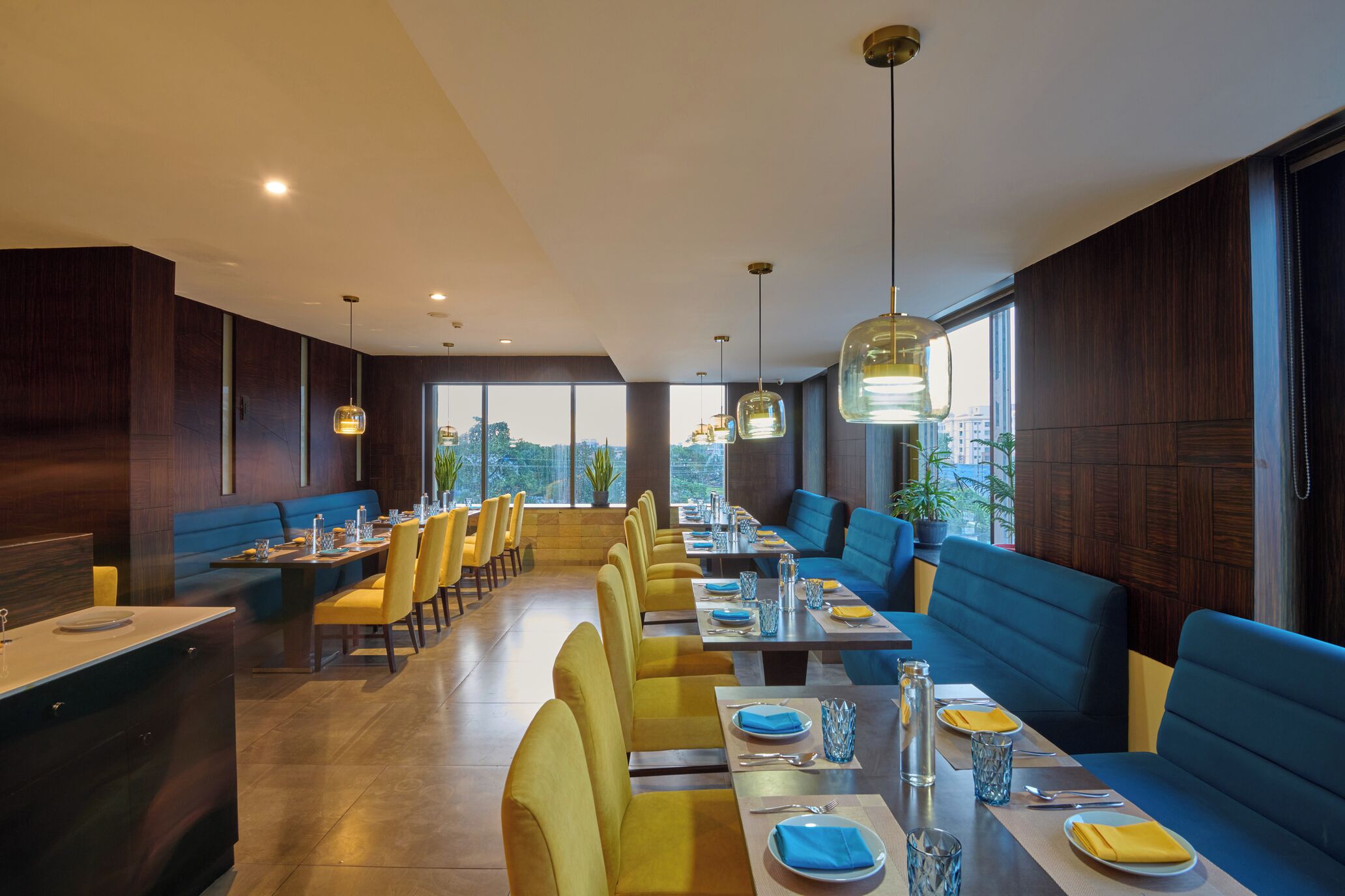 A modern restaurant with high ceilings, large windows, and a mix of yellow and blue seating.
