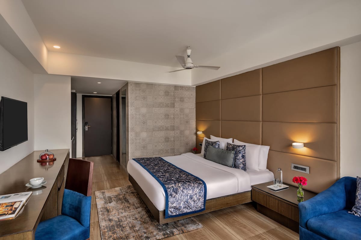 A modern hotel room with a large bed, a desk, a chair, and a TV.