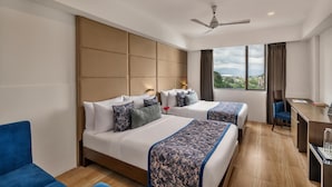 A hotel room with two beds, a desk, a chair, and a view of the outdoors. - Voyage Milestone Hotel & Banquet Siliguri (Jalpaiguri)
