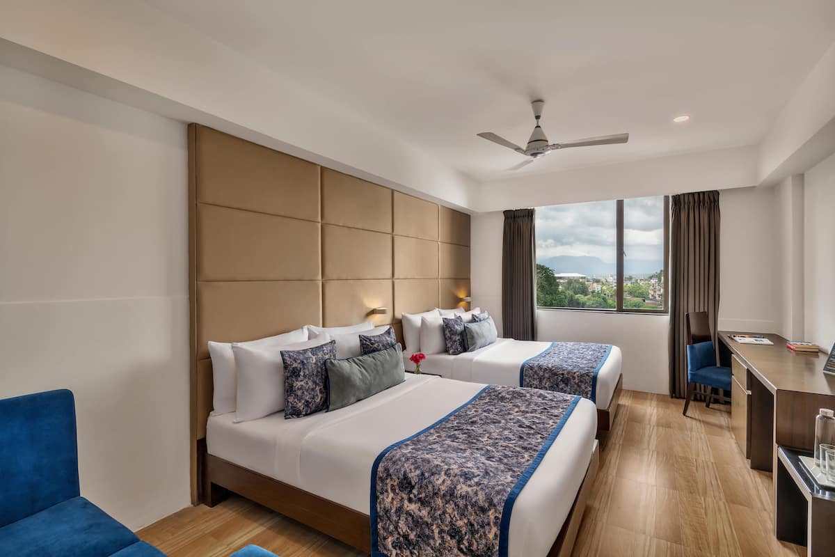 A hotel room with two beds, a desk, a chair, and a view of the outdoors.
