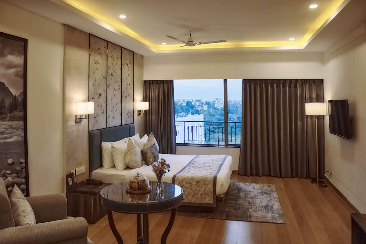 A modern hotel room with a large bed, a sofa, a coffee table, and a TV.