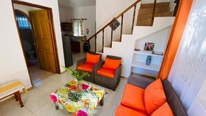 Un salon avec un canapé, une table basse recouverte d’une nappe à motifs floraux et un escalier menant à l’étage supérieur.