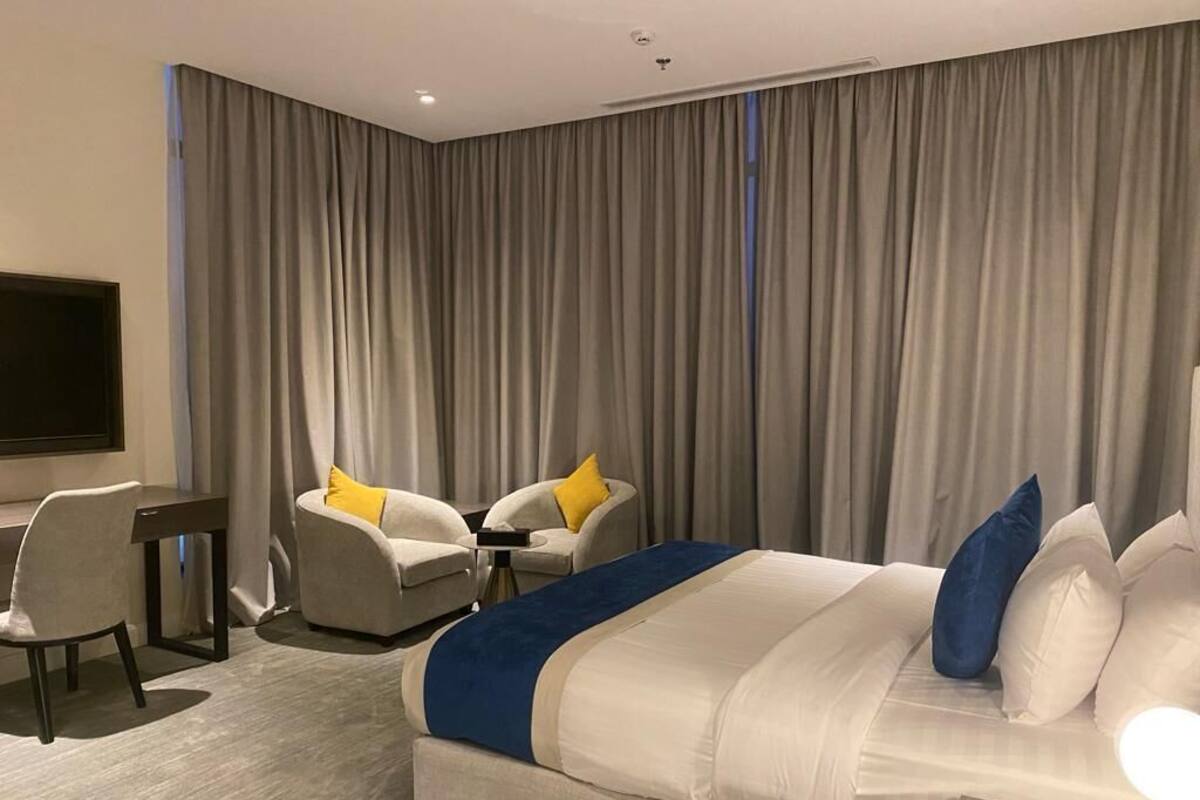 A hotel room with a large bed, a desk, two chairs, and a TV.