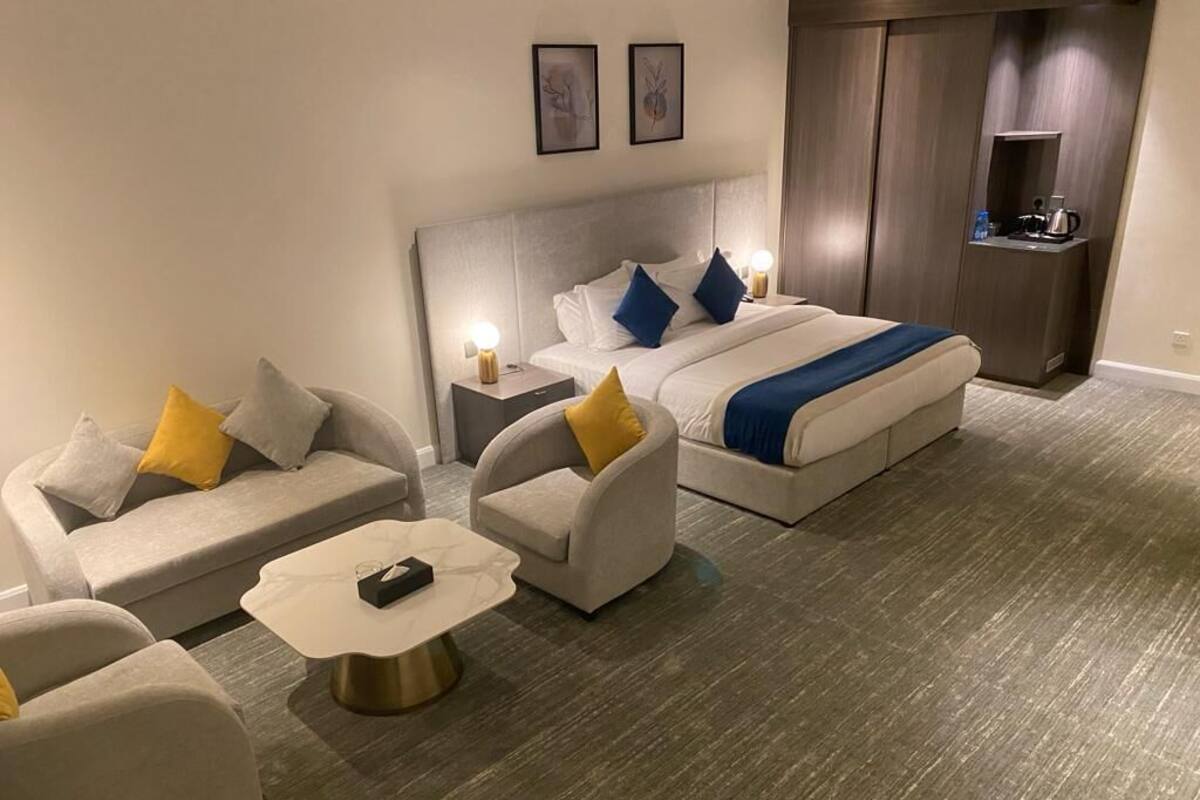 A hotel room with a bed, two sofas, a coffee table, and a nightstand with a lamp.