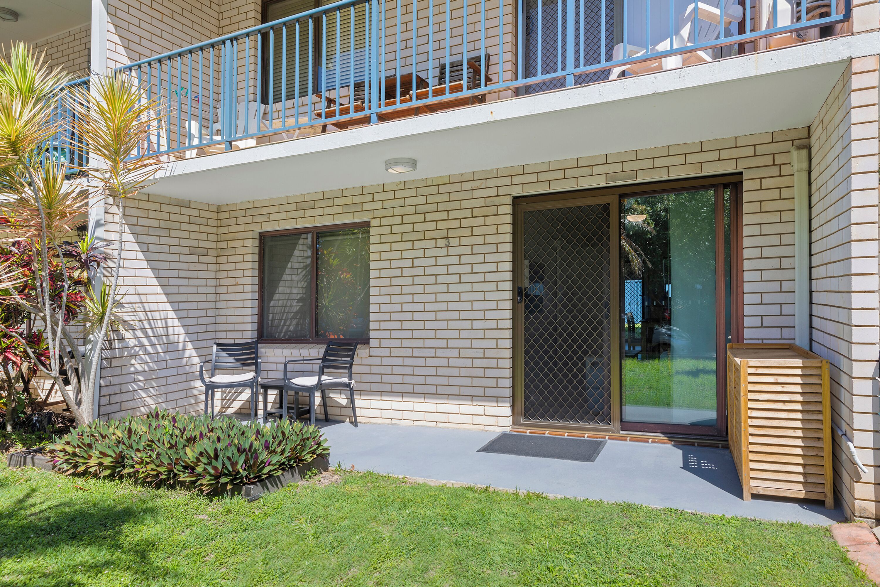 A two-story building with a balcony, a sliding glass door, and a small patio area with a table and chairs.