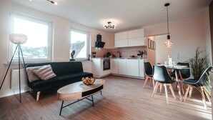 Un salon moderne avec un canapé noir, une table basse en bois et un coin repas comprenant des chaises noires et une table en bois.