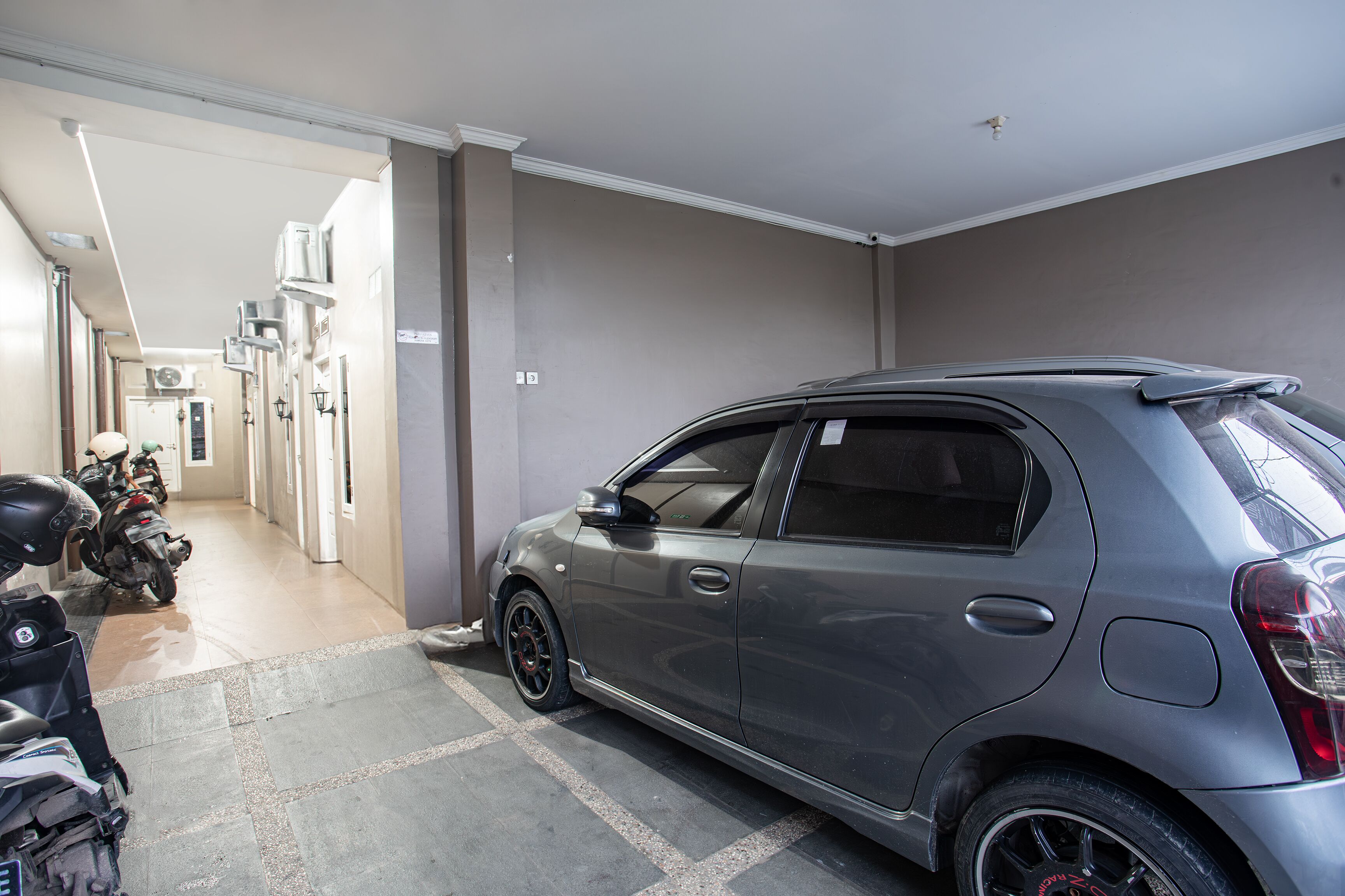 Un garaje para estacionamiento con un coche gris y motocicletas.