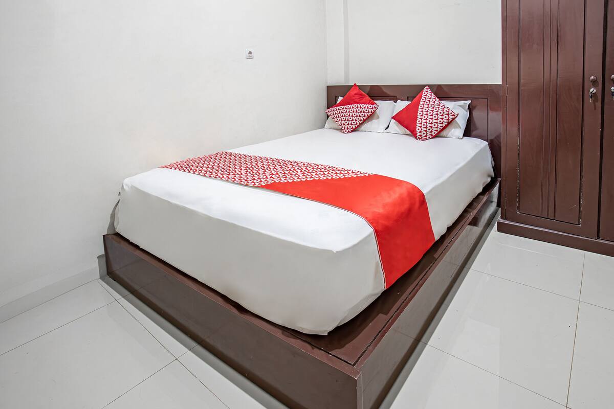A neatly made bed with a white and red bedspread, a wooden headboard, and matching pillows.
