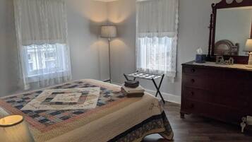Une chambre à coucher avec un lit, une commode, une lampe et une fenêtre avec des rideaux.