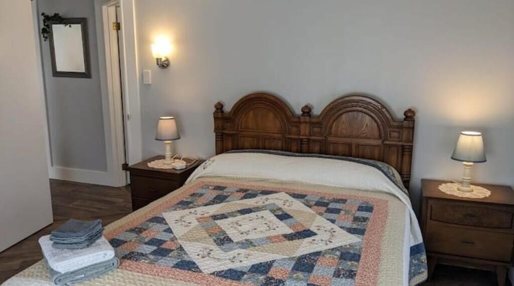 Un letto rifatto con copriletto, due comodini con lampade, uno specchio a parete e una porta.