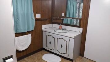 A bathroom with a white sink, wooden cabinets, a mirror, and a white towel on the floor.