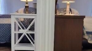A room with a wooden floor, a white pillar, and two nightstands with lamps.