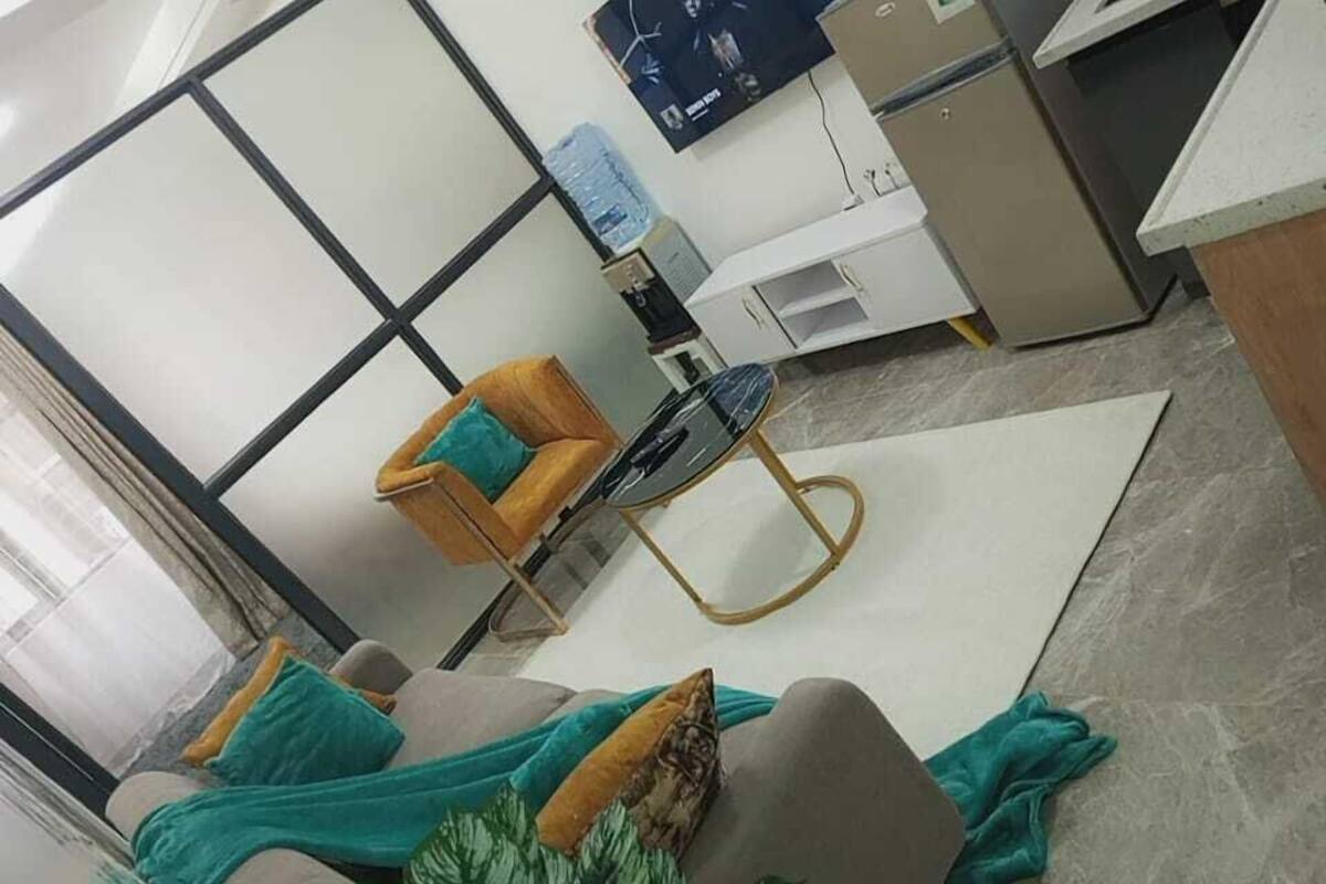 A modern living room with a sofa, a round table, and a chair. There is a water dispenser and a television on the wall.
