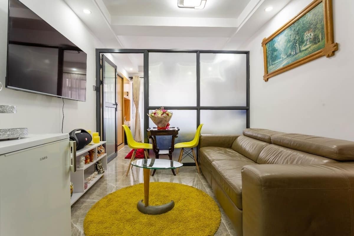 A compact living space with a sofa, a small table with chairs, a TV, and a painting on the wall.