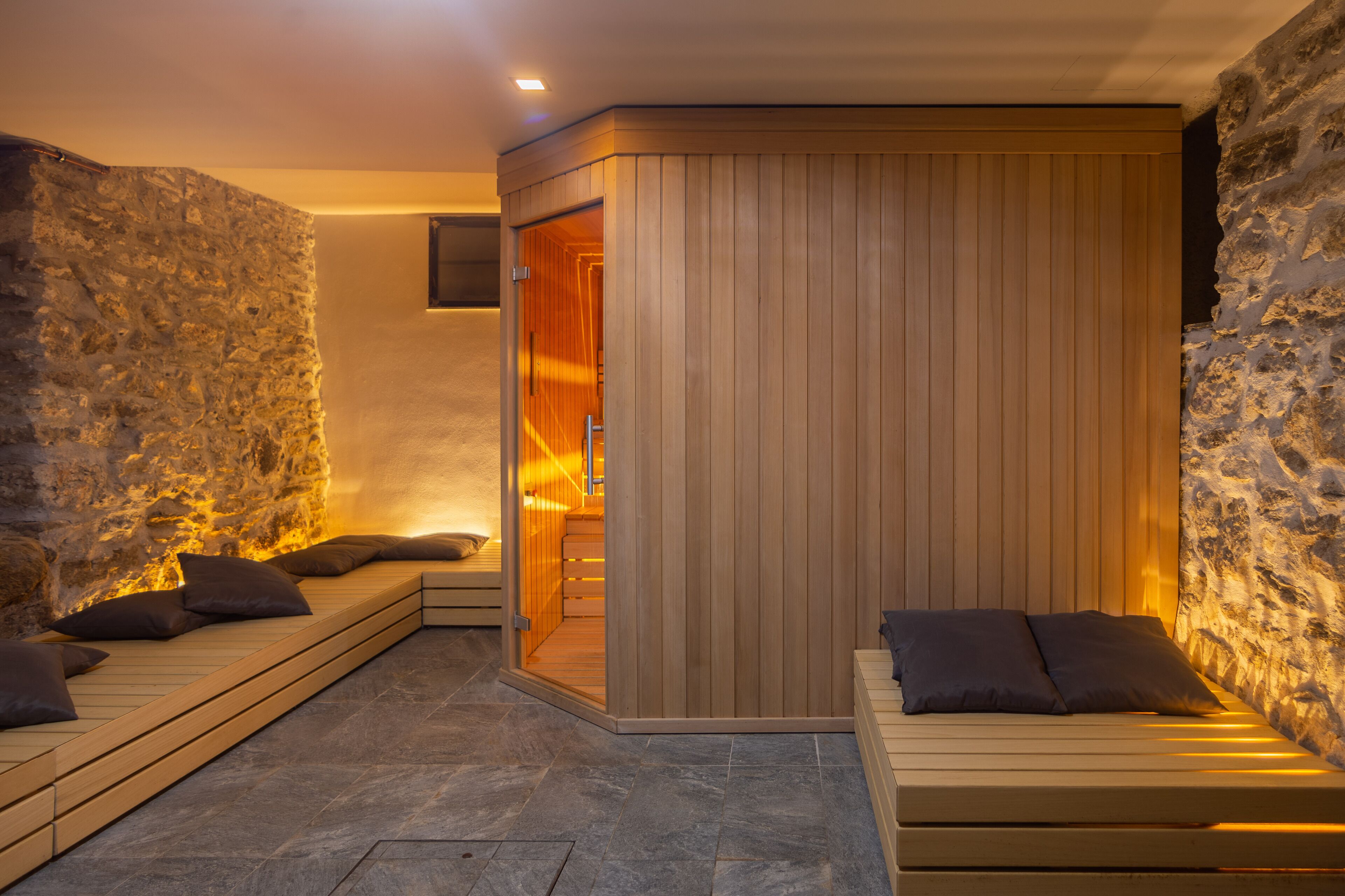 A spa room with a stone wall, wooden benches, and a wooden partition.
