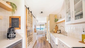 A modern kitchen with a coffee maker, a chalkboard with 'Aloha' and a heart, wooden flooring, and a view to a balcony. - Chic Oceanfront Escape-Boutique Studio-Noelani 219-Cold AC-Amazing Ocean View (Lahaina)