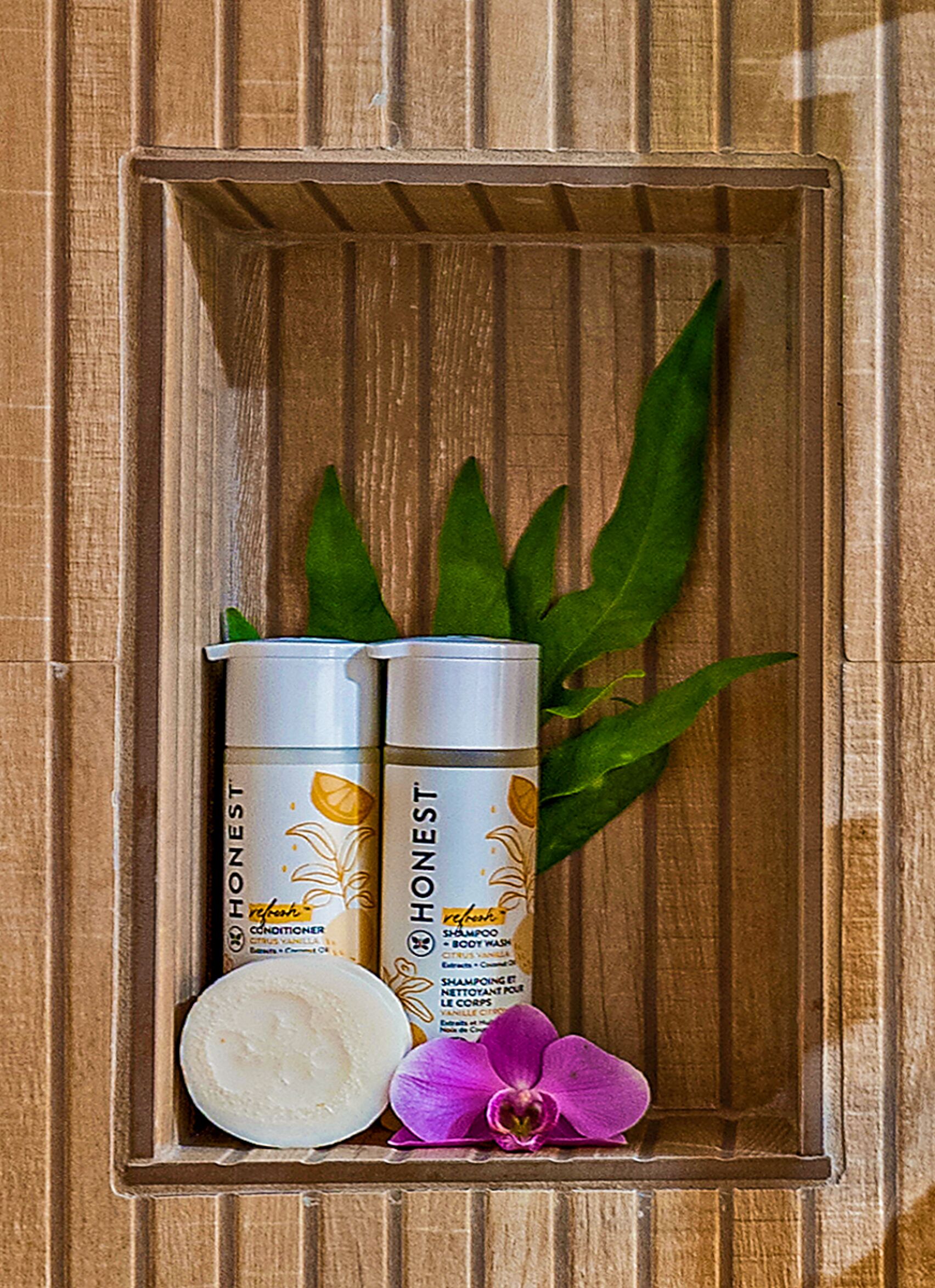 Two bottles of Honest shampoo and conditioner, a white soap bar, and a purple orchid.