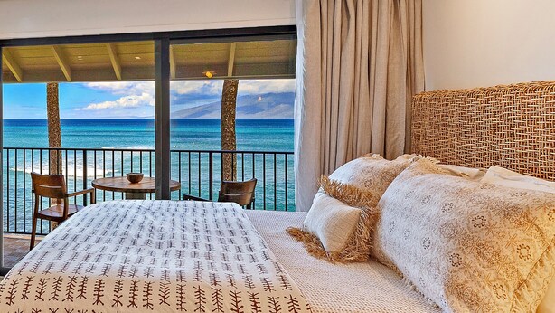 A hotel room with a large bed, a balcony with a view of the sea, and a wicker headboard. - Chic Oceanfront Escape-Boutique Studio-Noelani 219-Cold AC-Amazing Ocean View (Lahaina)