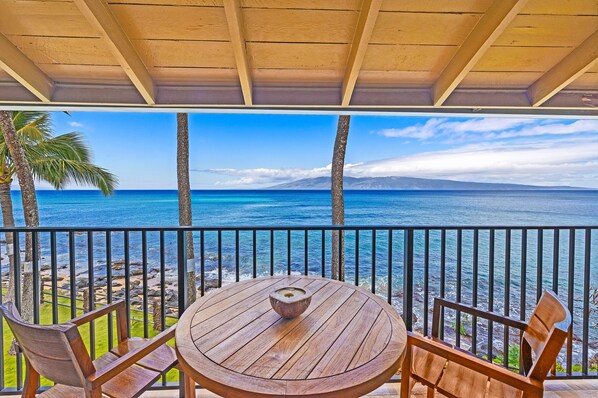 A wooden table and chairs on a balcony with a view of the ocean and a mountain in the distance.