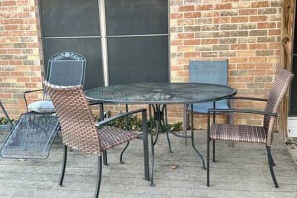 An outdoor patio with a round metal table and four wicker chairs.