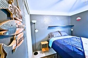 Een slaapkamer met een bed, nachtkastje, lamp en wanddecoraties, waaronder een bordje met de tekst 'Gone Fishin''.