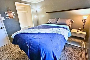 A bedroom with a bed, bedside table, lamp, and a wall-mounted sign.