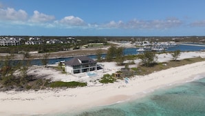 A beachfront property with a modern house, a marina with boats, and clear turquoise waters. - Beachfront estate home with private 70’ dock and 7500sq ft. of living space (Exuma)