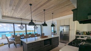 A modern kitchen with a large island, dark cabinetry, and a view of the ocean. - Beachfront estate home with private 70’ dock and 7500sq ft. of living space (Exuma)