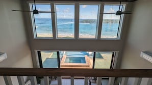 A room with large windows overlooking a beach and a pool area. - Beachfront estate home with private 70’ dock and 7500sq ft. of living space (Exuma)