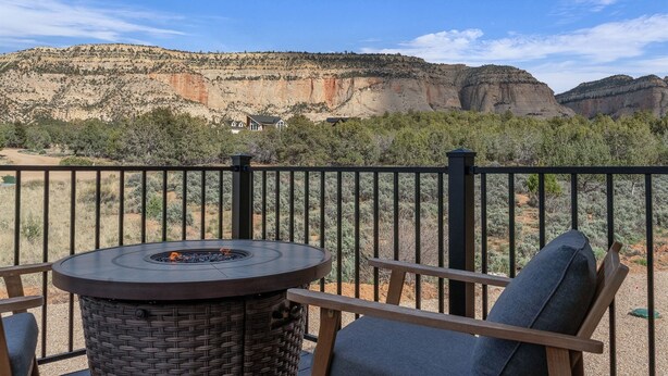 Eine Terrasse mit rundem Tisch und Stühlen, mit Blick auf eine gebirgige Landschaft.