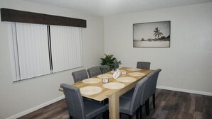 A dining area with a wooden table, grey chairs, and a plant centerpiece.