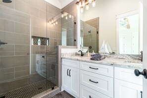 A modern bathroom with a glass shower enclosure, white cabinetry, and a large mirror.